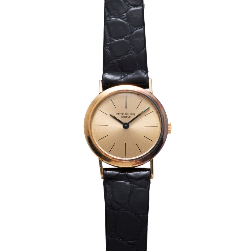 Gold-toned round watch with champagne dial, applied indices, and black crocodile leather strap.