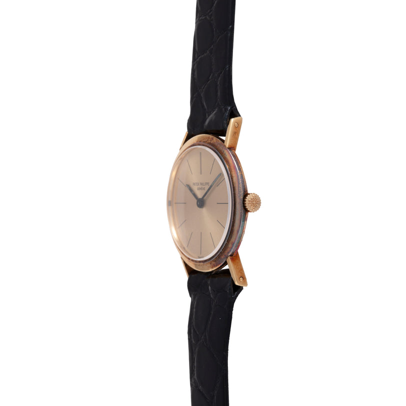 Gold-tone oval watch with champagne dial, applied hour markers, and black leather strap.