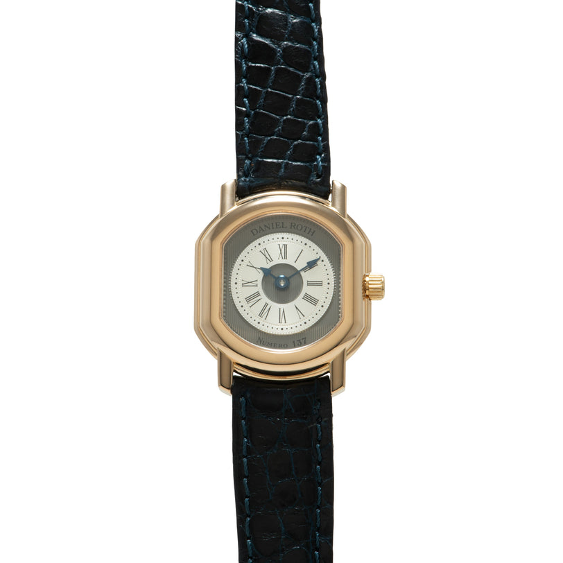 Gold-tone square watch with cream dial, Roman numerals, and dark blue crocodile leather strap.