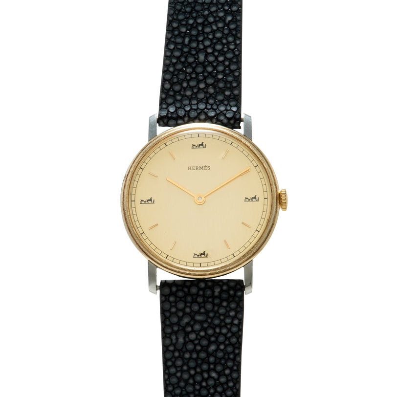 Hermès watch with cream dial, gold-tone case, gold hands, and black textured leather strap.