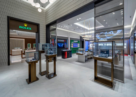 Modern luxury watch store interior with Rolex and Tudor displays, glass cases, and bright lighting.