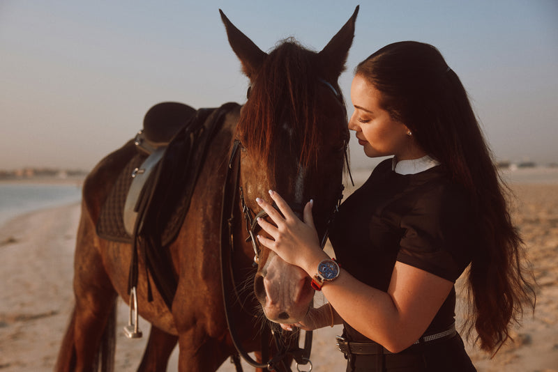 Audrey Raffy stands by the face of a horse on a beach