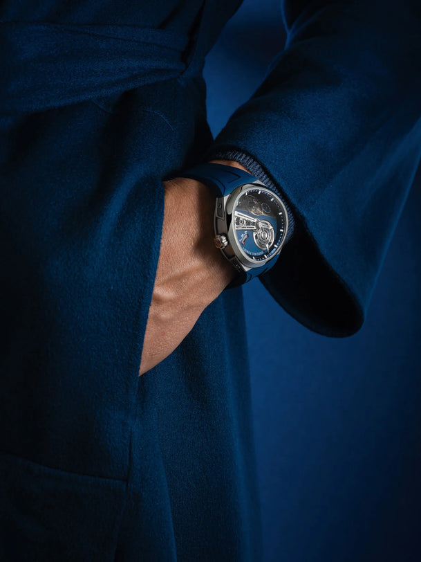 Titanium watch with blue dial and dark rubber strap worn on wrist over blue fabric.