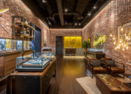 A modern luxury watch store with exposed brick walls, glass display cases, and leather seating.