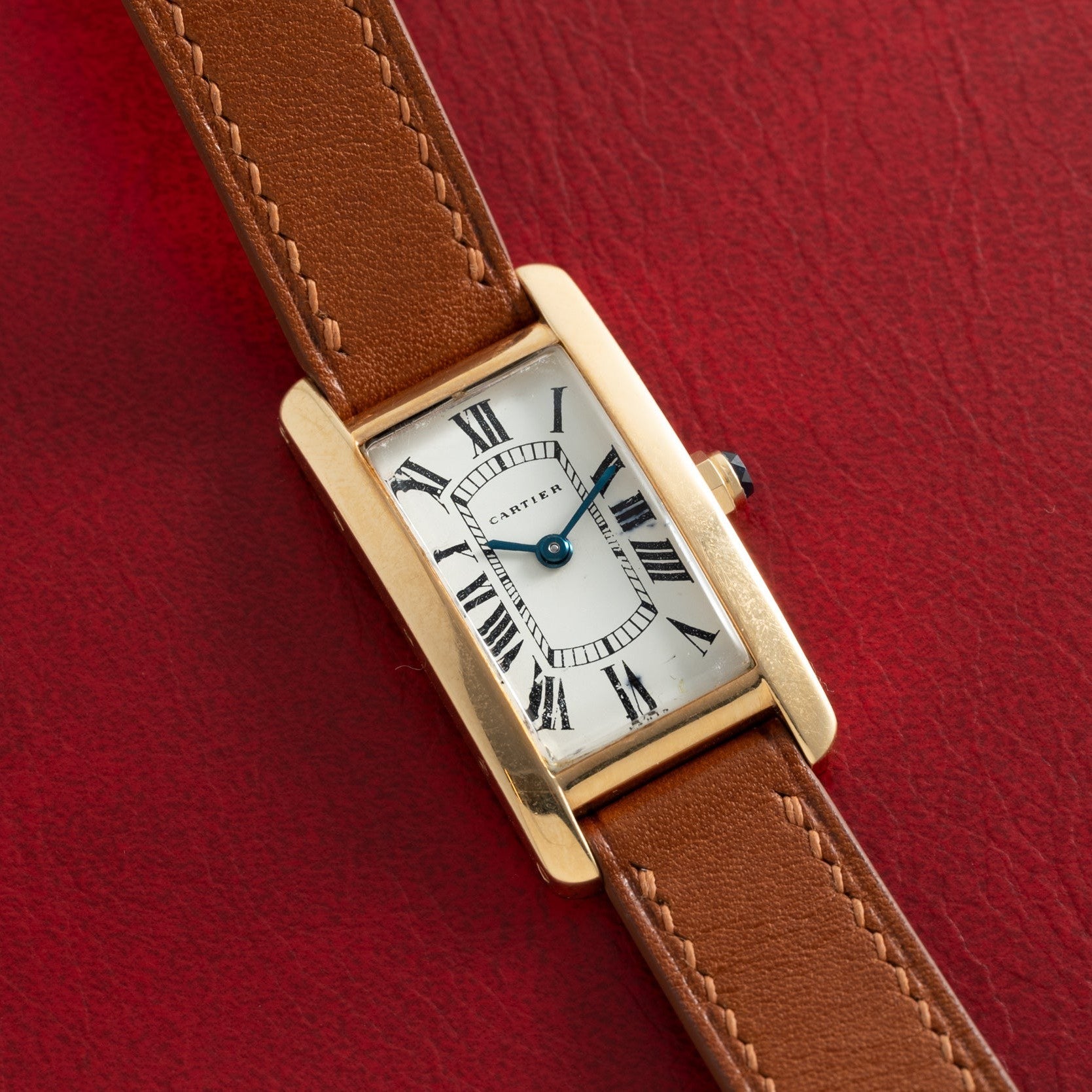 The Cartier Tank Cintrée Ladies watch with a brown leather strap is displayed on a red textured background.