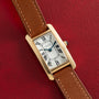 The Cartier Tank Cintrée Ladies watch with a brown leather strap is displayed on a red textured background.