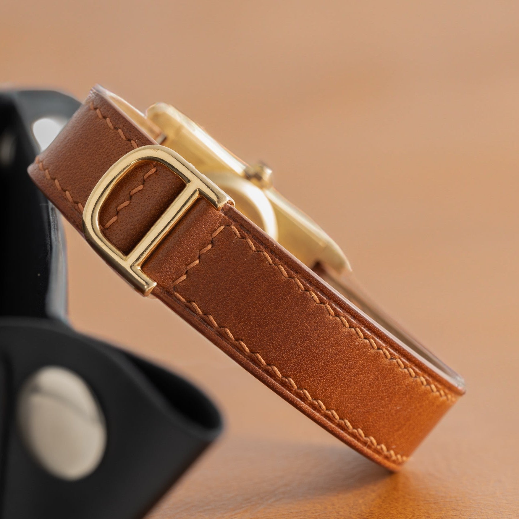 Close-up of the Cartier Tank Cintrée Ladies watchs brown leather strap with gold buckle on a beige surface.