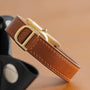 Close-up of the Cartier Tank Cintrée Ladies watchs brown leather strap with gold buckle on a beige surface.