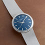 The Patek Philippe Calatrava Backwind, a silver wristwatch with a blue face and silver markers, is placed on a brown textured surface.