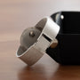 A Patek Philippe Calatrava Backwind with a silver mesh band and open clasp rests beside a black tray on a wooden surface.