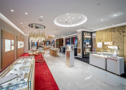 Luxury jewelry and watch store with glass display cases, bright lighting, and red carpet accents.