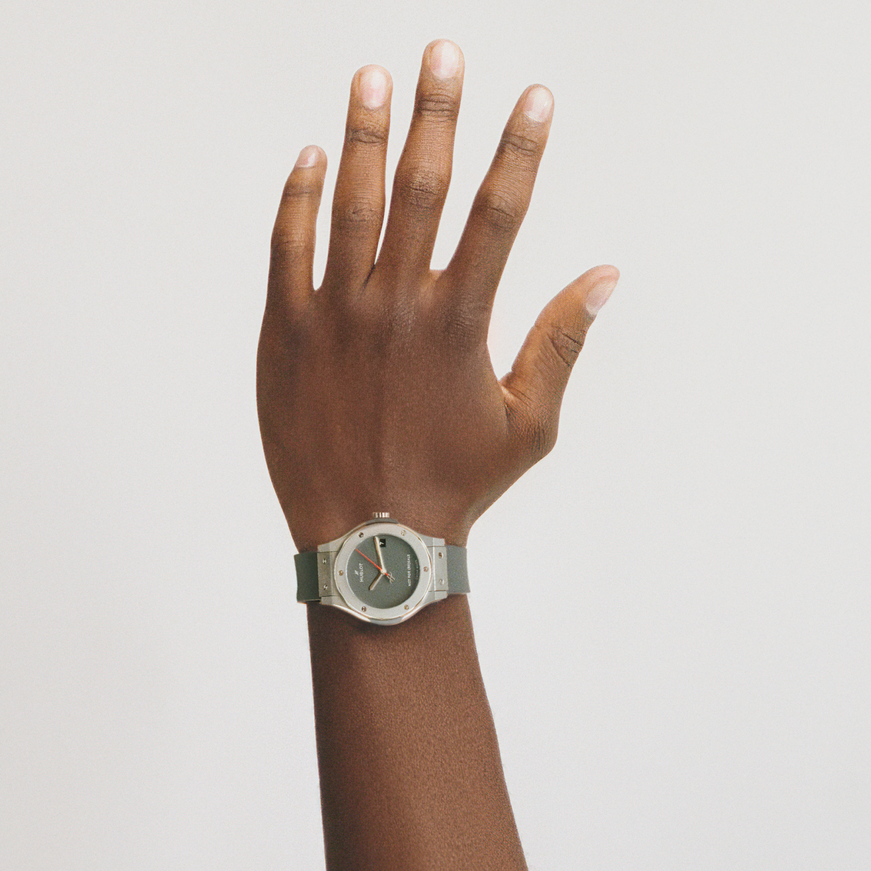 A hand with dark skin is raised against a white background, wearing the Hublot Classic Fusion Titanium Limited Edition for Hodinkee watch, which features a sleek silver strap and a dark face.
