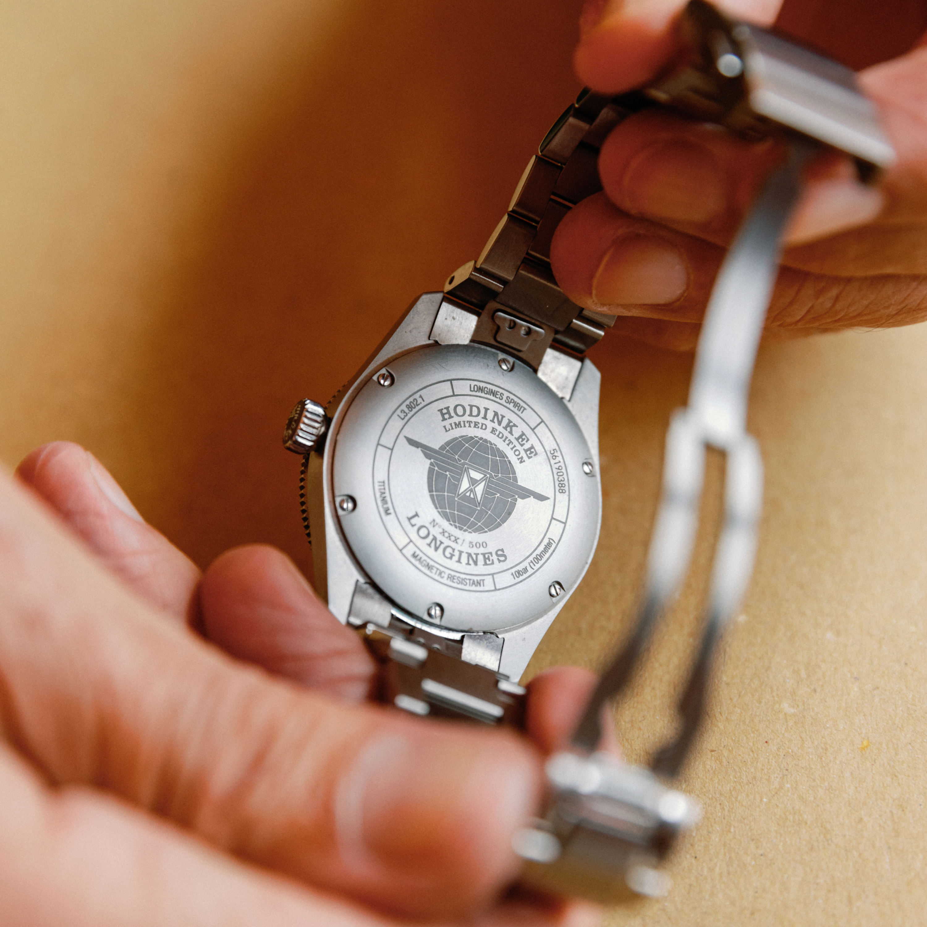 A person holds a metal wristwatch, showcasing the engraved case back that reads Longines Spirit Zulu Time Limited Edition for Hodinkee by Longines.