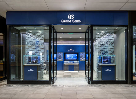 Grand Seiko store with blue signage, glass entrance, and brightly lit interior displaying watches.