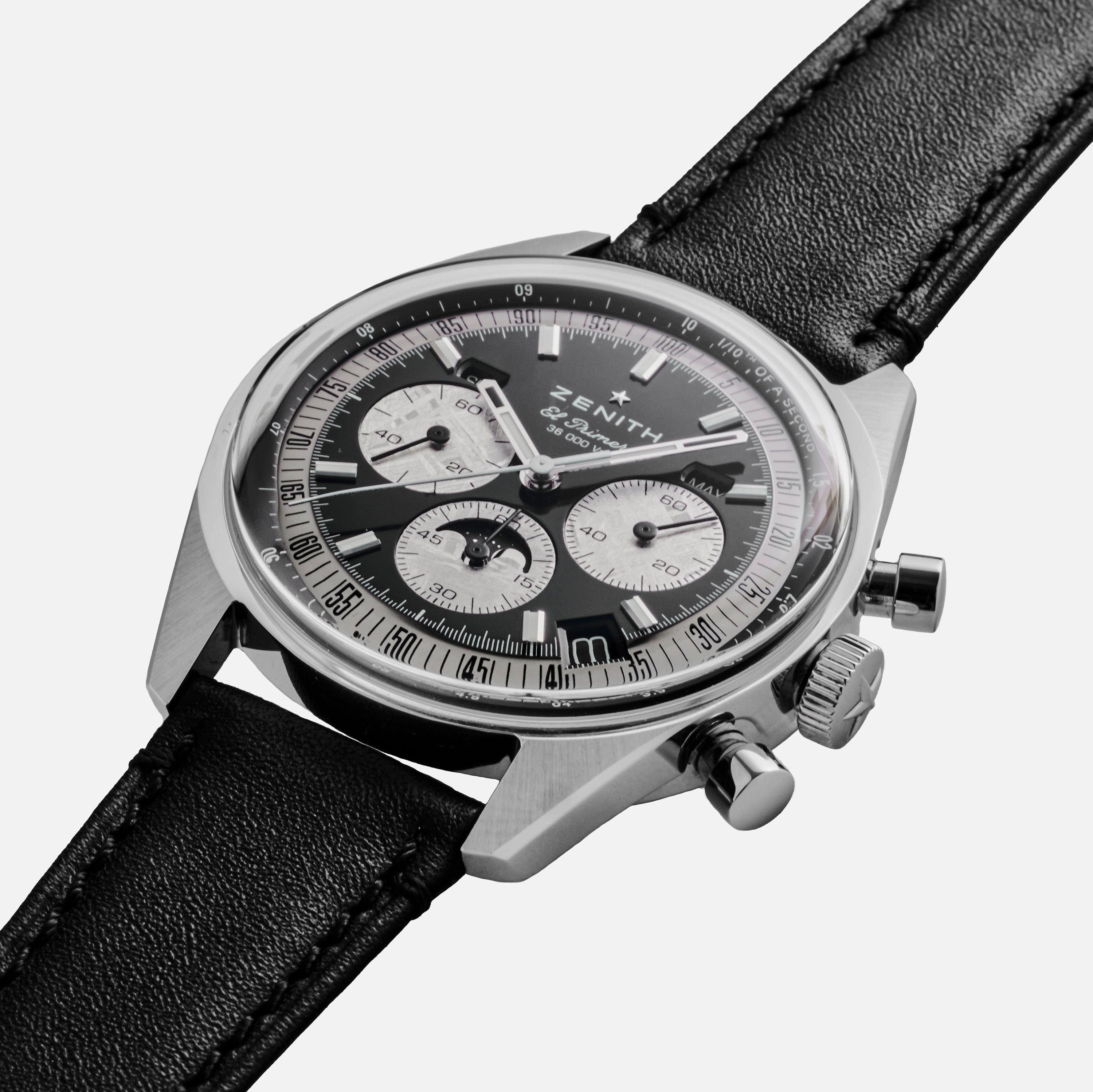 The Zenith Chronomaster Original Triple Calendar Limited Edition For Hodinkee features a modern chronograph design with a black leather strap, black and silver dial with three subdials, shown on a white background.