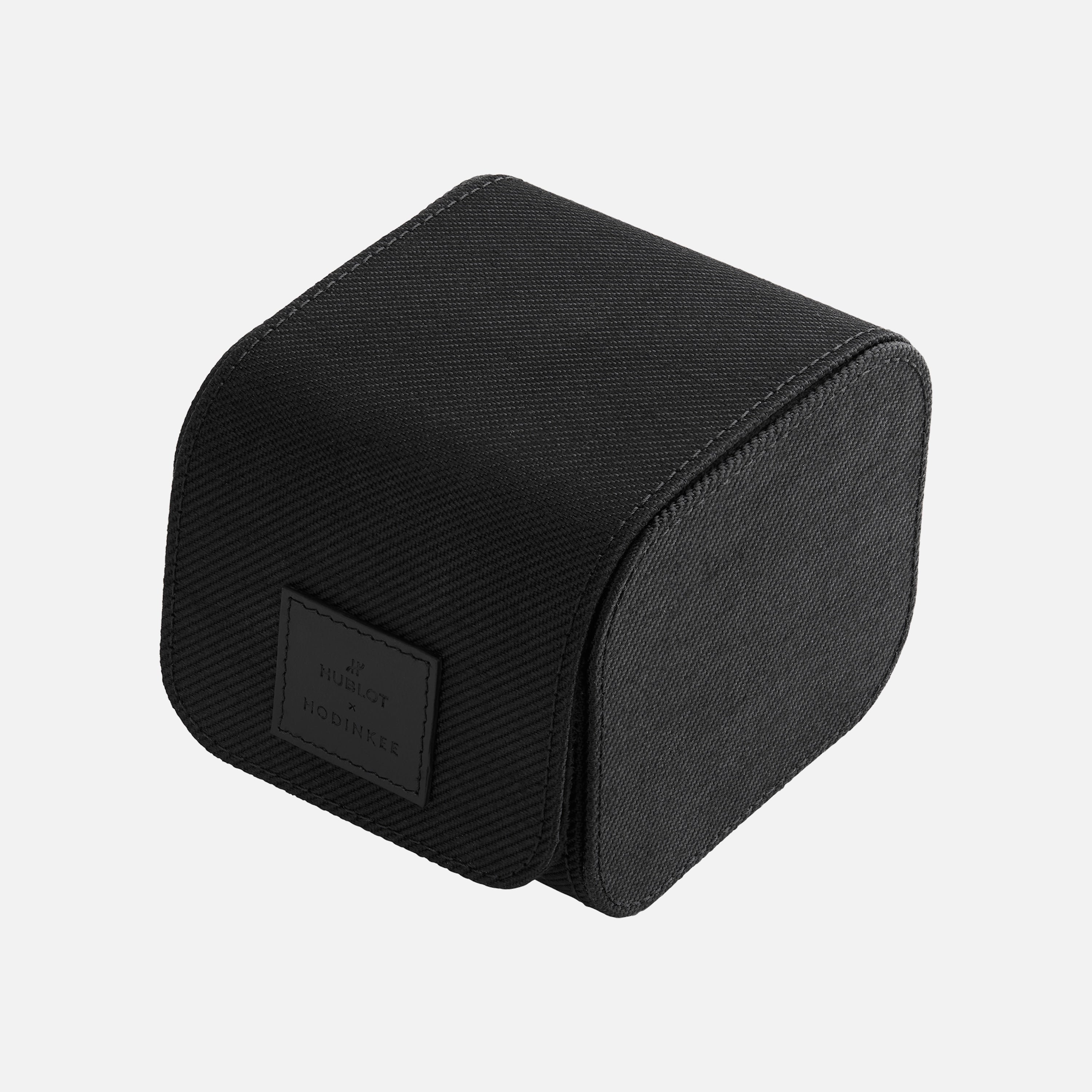 Sleek black rectangular fabric-covered watch box with curved front and “Hublot Boutique” label, designed for the Hublot Classic Fusion Titanium Limited Edition For Hodinkee. Shown against a plain white background.