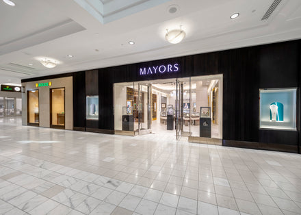Exterior view of MAYORS jewelry store in a shopping mall, with bright displays and glass doors.