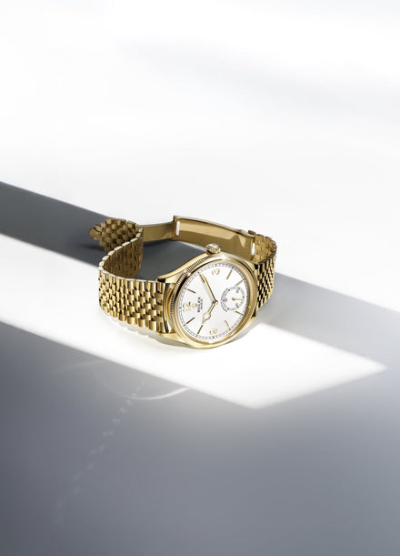 Gold Rolex 1908 watch on a grey and white geometric background