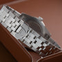 Close-up of a TUDOR Glamour Date silver bracelet and clasp resting on a brown leather surface.
