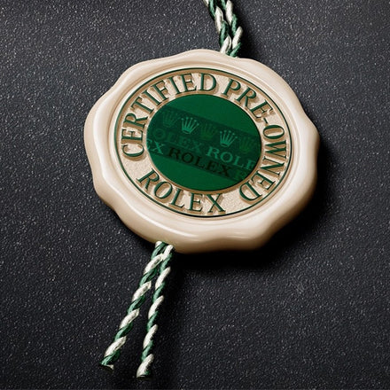 A green and cream Certified Pre-Owned Rolex tag with green and white string on a dark surface.