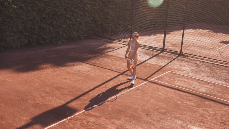 Dominique Schaefer stands at the back of a clay tennis court holding a racquet and ball