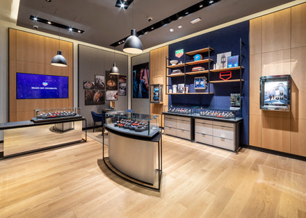 Modern watch store interior with glass display cases, wooden floors, and wall art showcasing watches and accessories.