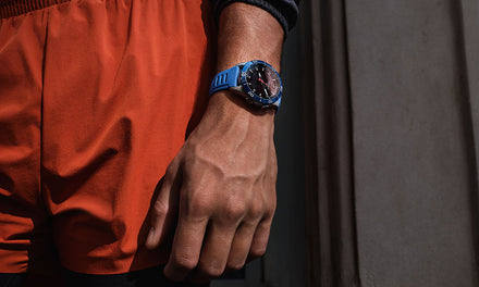 Close-up of a person wearing orange shorts and a blue wristwatch, standing near a wall.