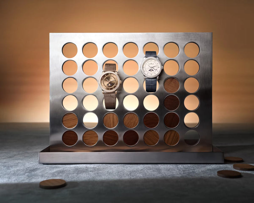 Brown gold watch with moon phase dial and dark leather strap displayed on metal color palette backdrop.