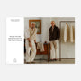 Two men in neutral outfits pose by a dresser and clothing rack in a minimal, stylish room, with Hodinkee Magazine, Volume 14 by Hodinkee displayed nearby.