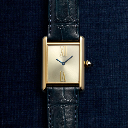 Gold rectangular Cartier watch with black leather strap on a dark textured background.