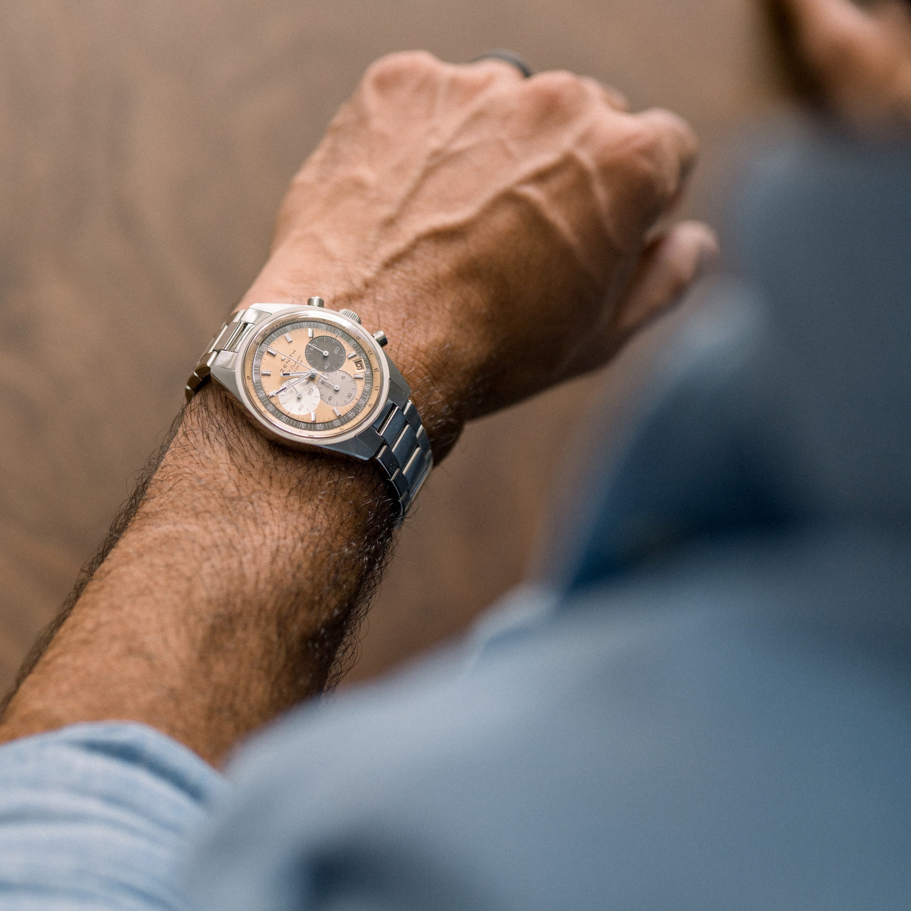 A close-up of a person’s wrist wearing the Zenith Chronomaster Original Limited Edition For Hodinkee, with classic silver and gold accents, resting on a surface, the watch face softly blurred in the foreground.