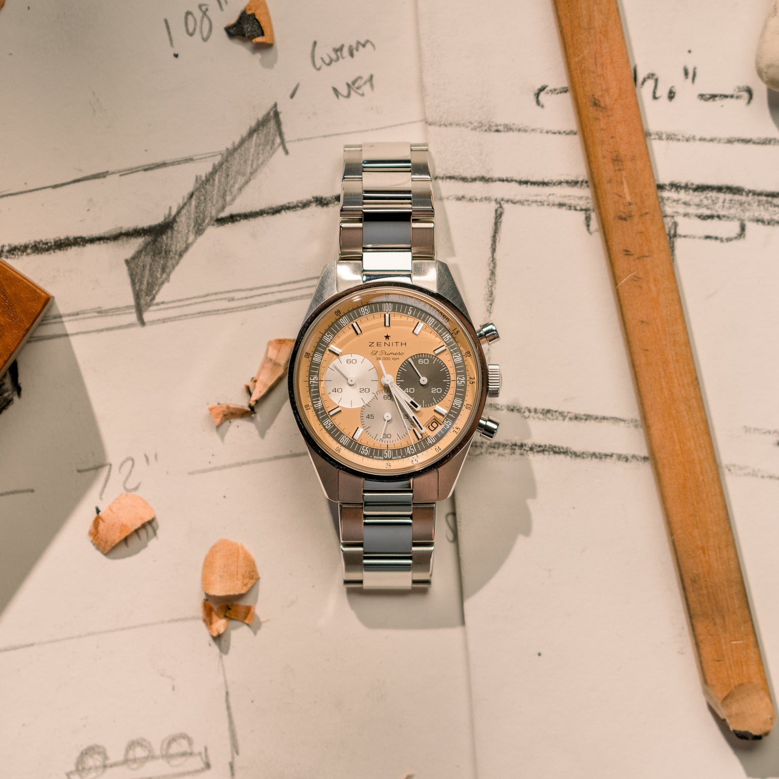 The Zenith Chronomaster Original Limited Edition For Hodinkee, featuring a cream and tan dial, rests on sketches with wooden pencils and shavings—a tribute to classic design.
