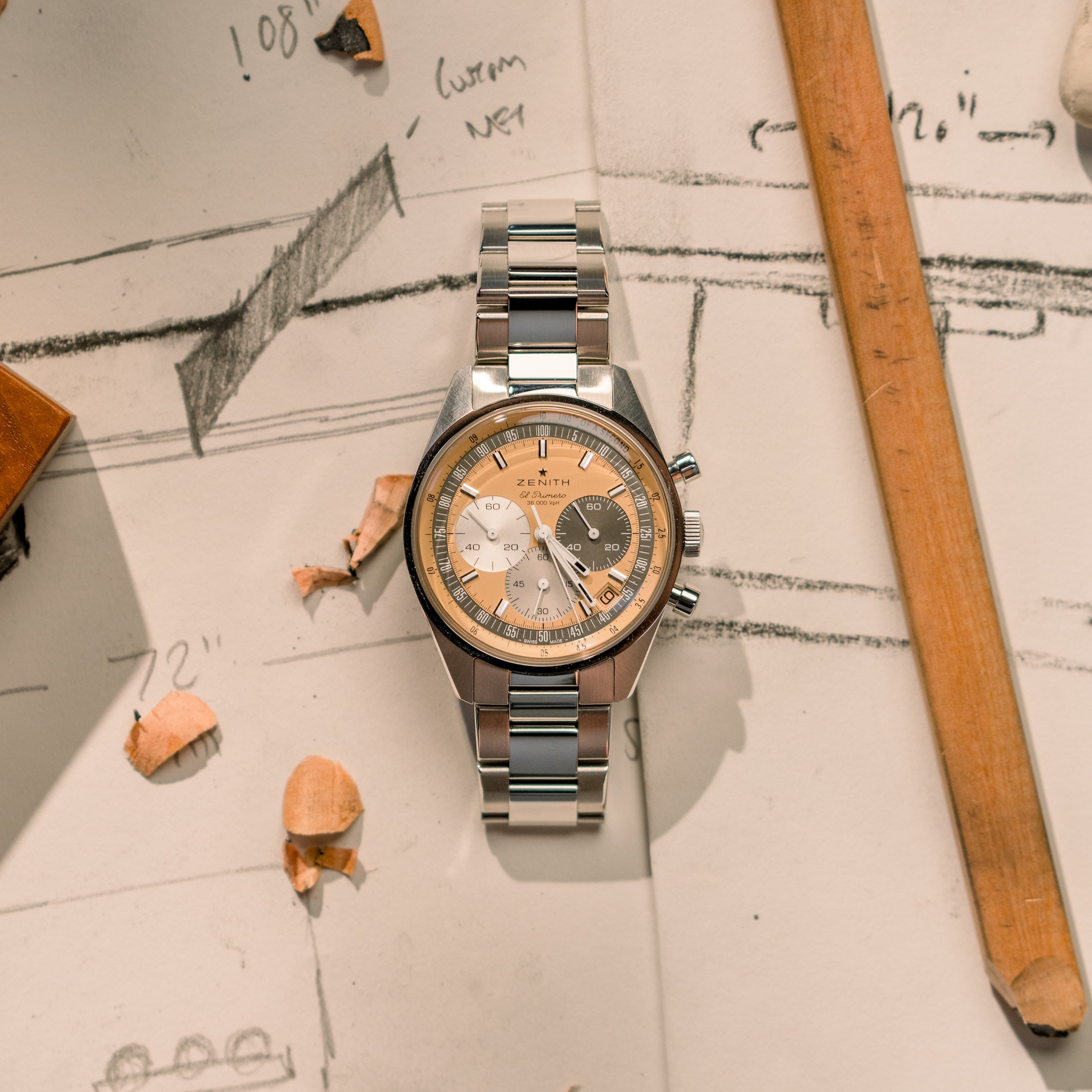 The Zenith Chronomaster Original Limited Edition For Hodinkee, featuring a cream and tan dial, rests on sketches with wooden pencils and shavings—a tribute to classic design.