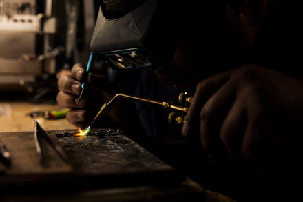 A welder in a helmet with a flame and tools working on a piece of jewelry