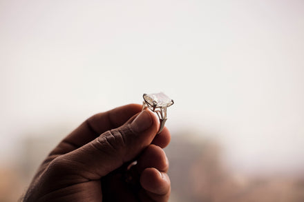A hand holds a ring against a blurry white background