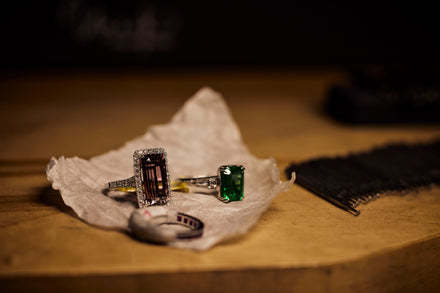 Two rings with colorful gemstones sit on a piece of paper and a brown background