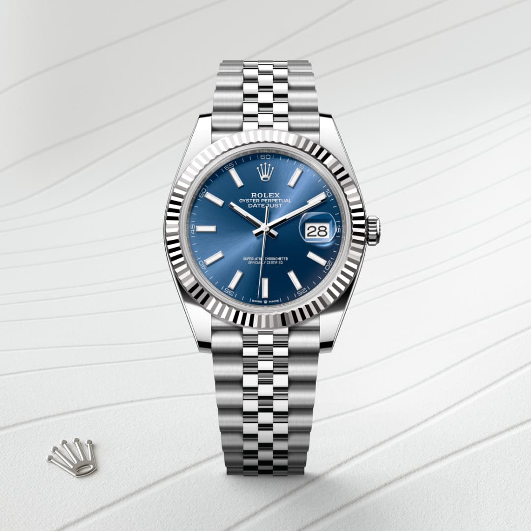Silver Rolex watch with blue dial and metal bracelet on a light textured background; crown logo beside it.