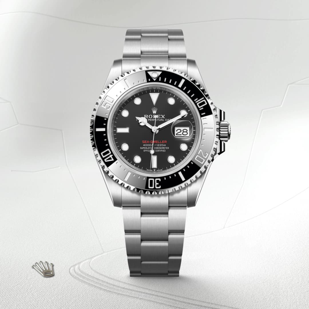 A silver Rolex Sea-Dweller watch with a black dial and date display, set against a light textured background.