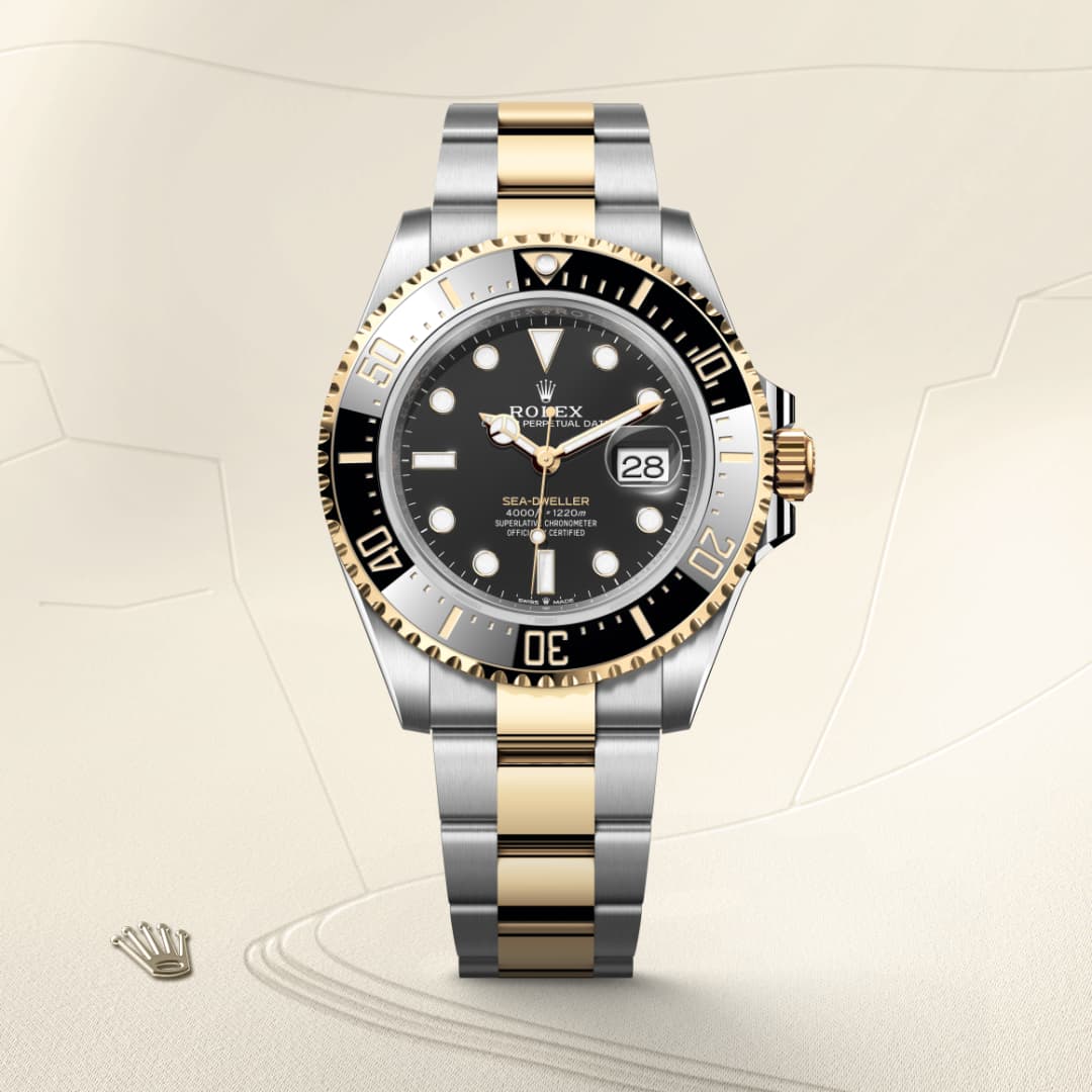 A Rolex Sea-Dweller two-tone wristwatch with a black dial on a light patterned background.