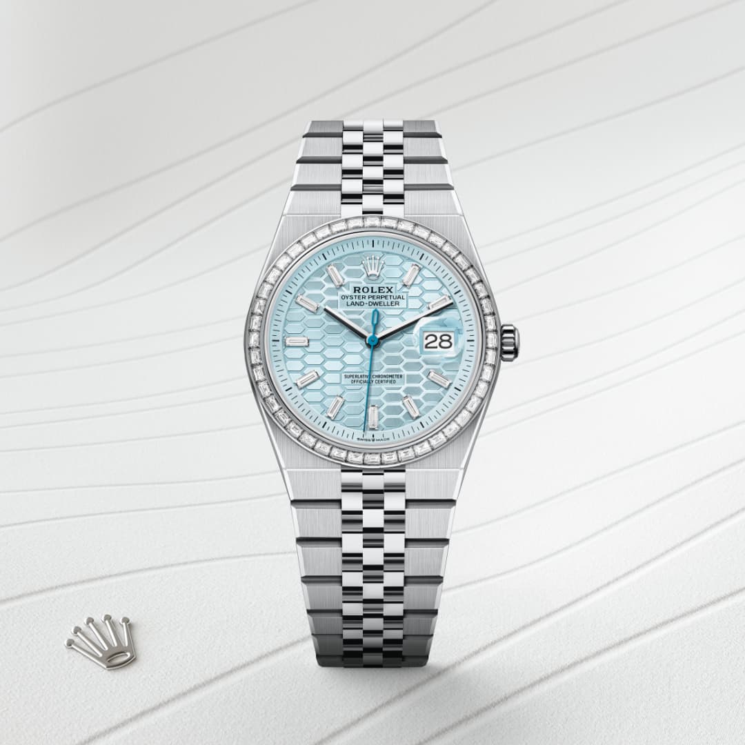 A silver Rolex watch with a blue patterned dial, date display, diamond bezel, and metal bracelet on a textured surface.