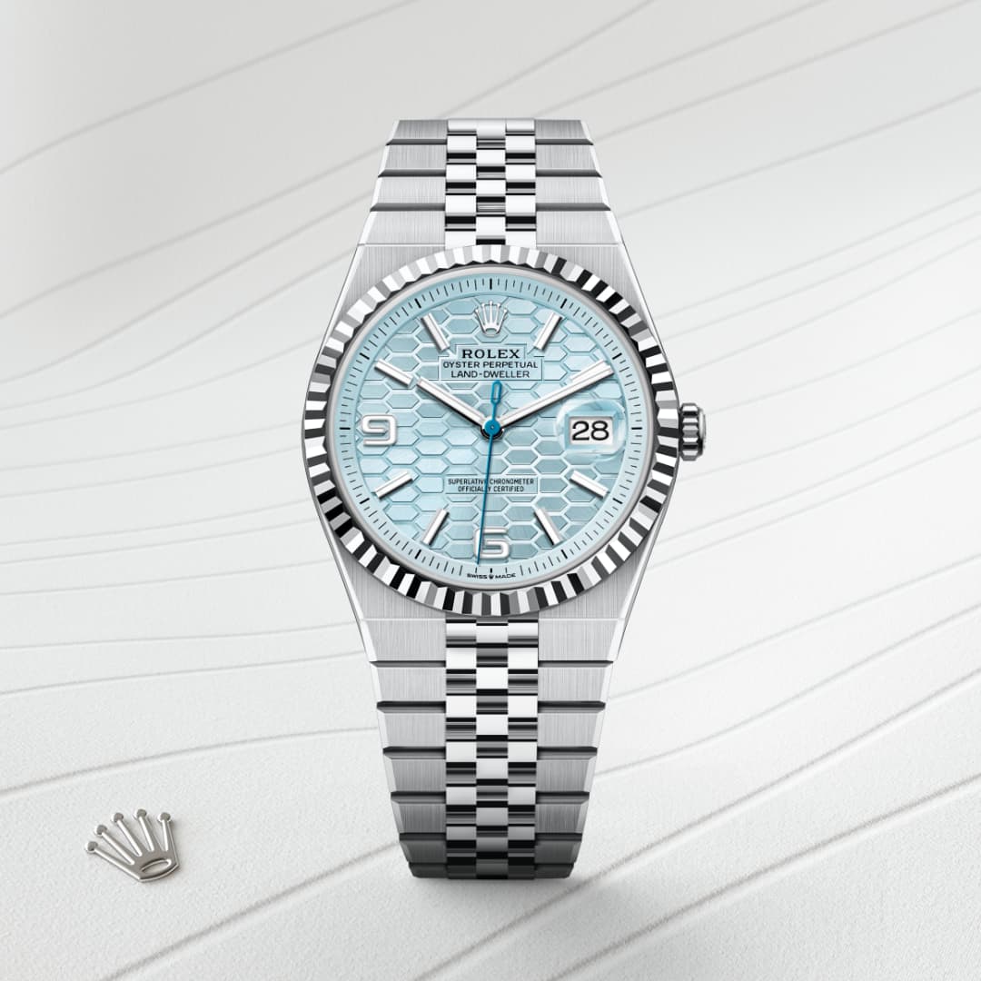 A silver Rolex watch with a blue patterned dial and date display on a textured white surface.