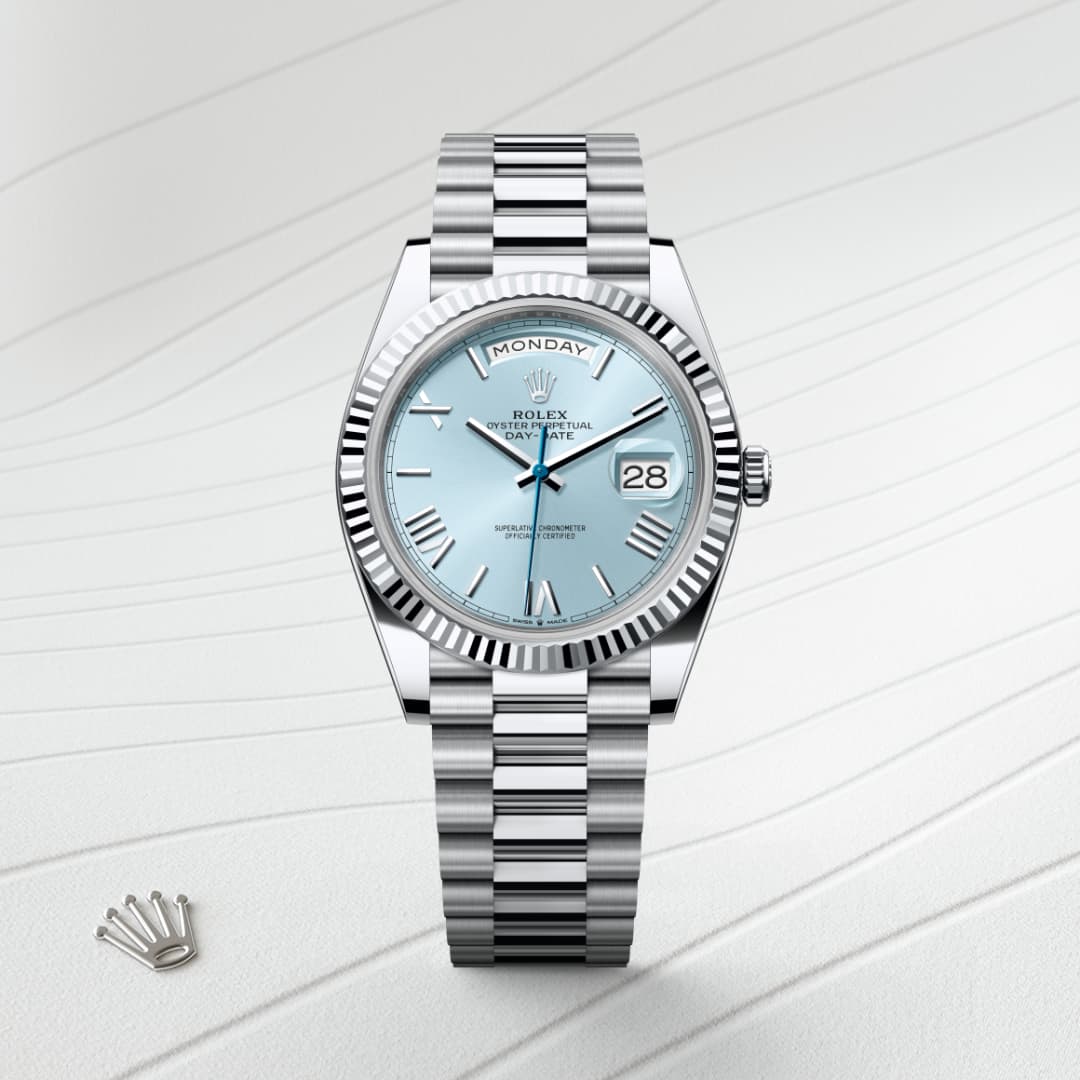 A silver Rolex watch with a light blue dial displays the day and date, set on a patterned white background.