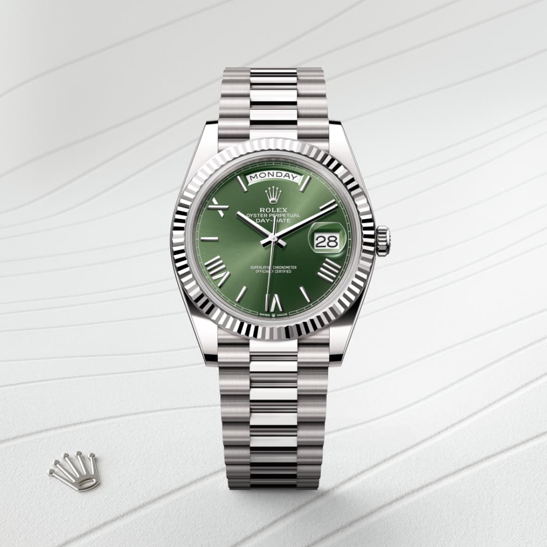 A silver Rolex watch with a green dial displays the day and date, set against a textured white background.