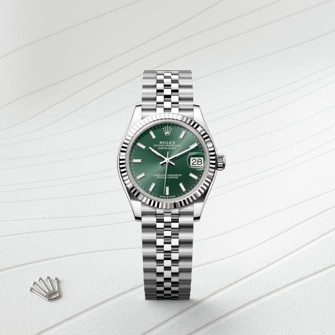A silver Rolex watch with a green face and date display, placed on a textured white surface.