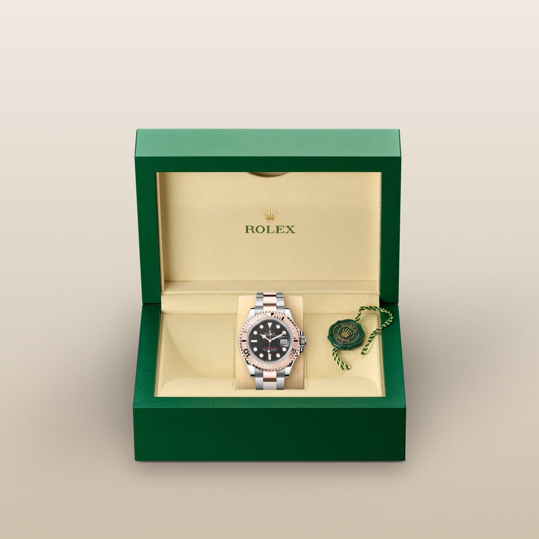 A Rolex watch with a black dial in a green and cream box, with a green tag beside it.