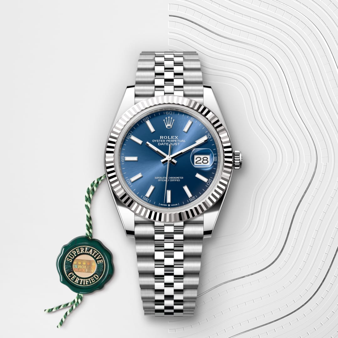 A Rolex Datejust watch with a blue dial, silver bracelet, and Superlative Certified green tag.
