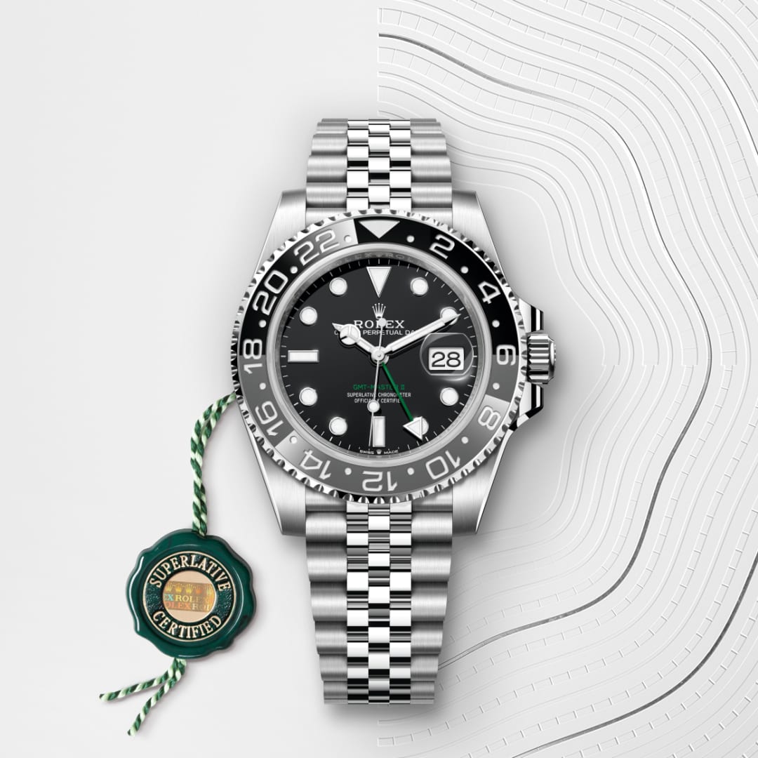 A Rolex GMT-Master II watch with a black dial and jubilee bracelet, next to a green Superlative Certified tag.