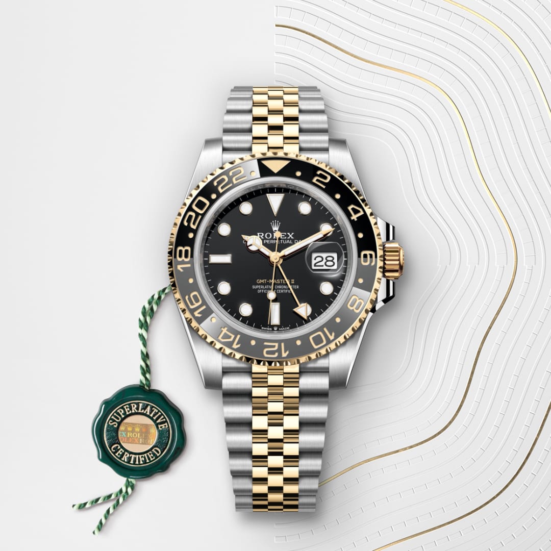 A two-tone Rolex watch with a black dial and date, next to a green Superlative Certified tag.