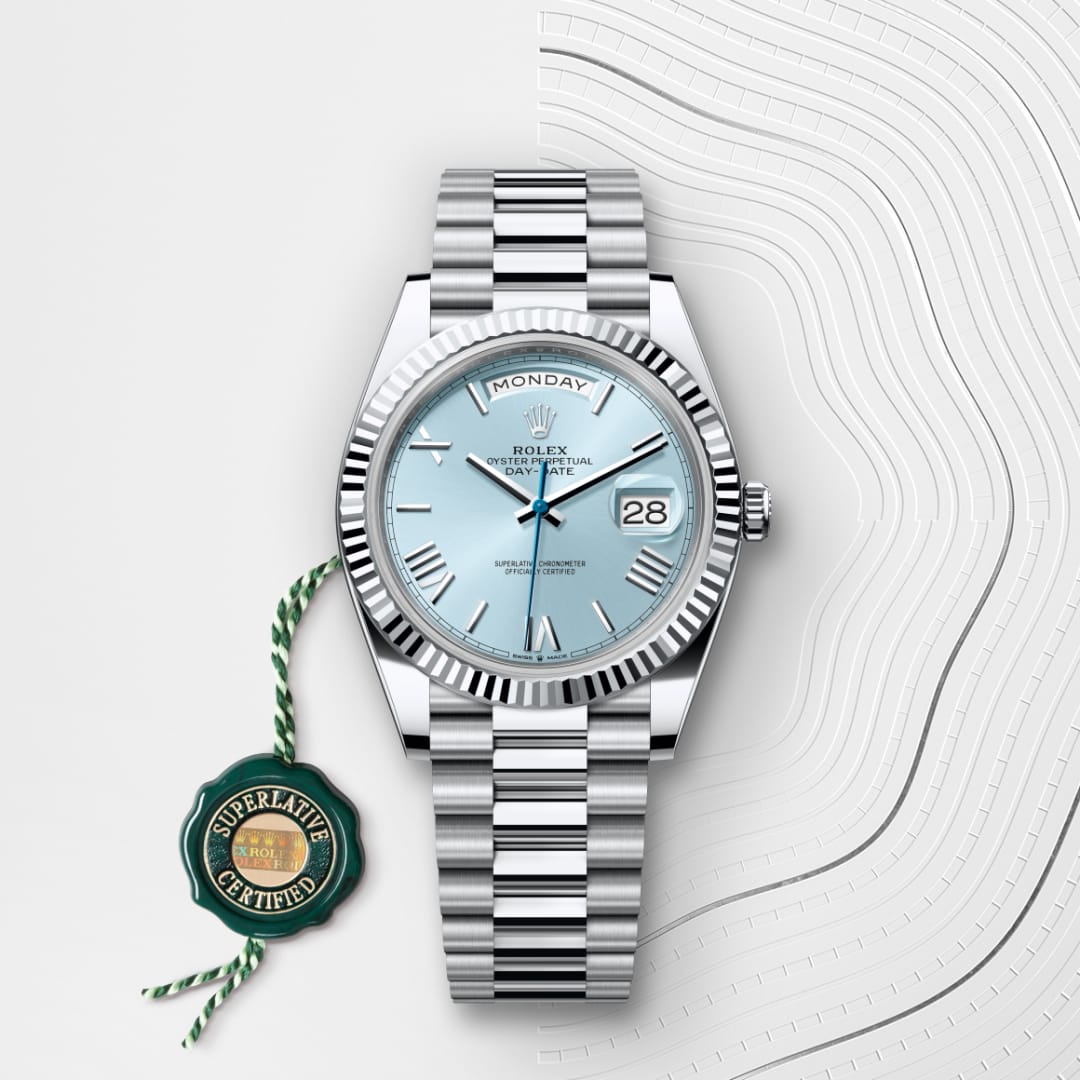 Silver Rolex watch with an ice-blue face and date display, beside a green Superlative Certified tag.