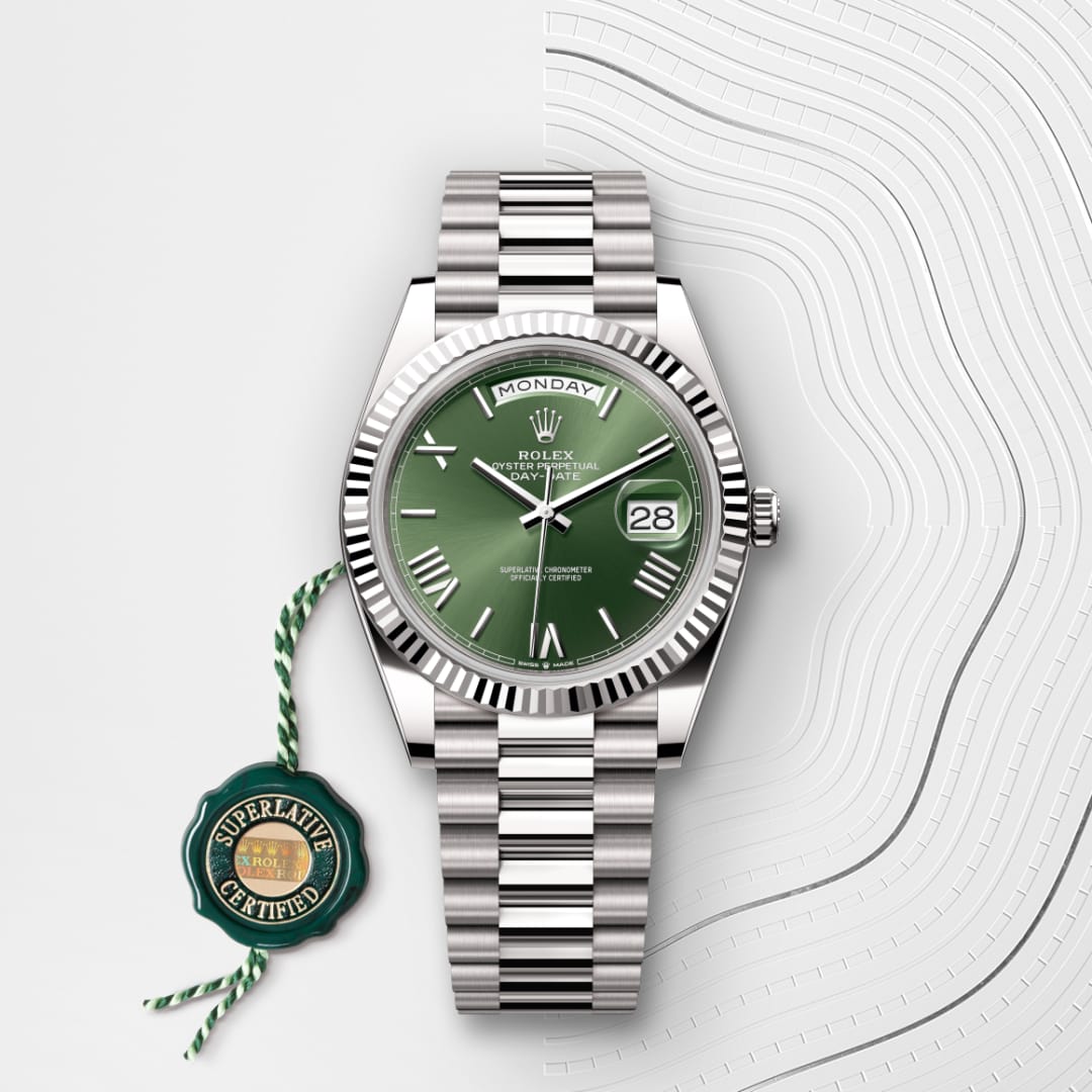 Silver Rolex watch with a green face showing Monday and 28, next to a “Superlative Certified” green tag.